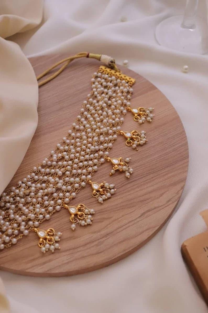 Puede incluir: Un collar de oro con m&uacute;ltiples hileras de perlas blancas y detalles dorados. El collar tiene varios colgantes con detalles de perlas.