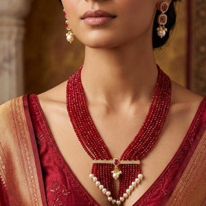 May include: A striking red beaded necklace with a pendant, red gemstone, and white pearls. Matching earrings with red gemstones and pearls are also visible. The jewellery is set against a red and gold fabric.
