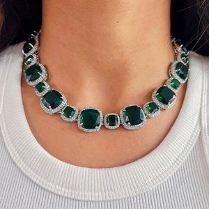 Puede incluir: Un collar de plata con grandes piedras de color verde esmeralda engastadas en forma cuadrada. Las piedras están rodeadas de piedras más pequeñas y transparentes.