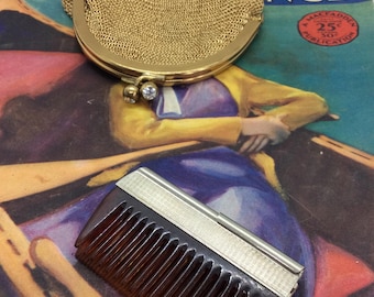 May include: A vintage gold mesh coin purse with a clasp and a brown comb with a silver accent. The items rest on a vintage magazine cover with the words "Dream World" and "September".