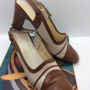 Puede incluir: Un par de zapatos de tacón slingback vintage en marrón y beige. Los zapatos tienen un tacón de bloque y una correa en el tobillo con hebilla. La marca "Norvic Celebrity" es visible en el interior.