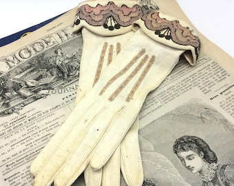 May include: A pair of off-white gloves featuring decorative cuffs with scalloped embroidery in shades of pink, brown, and black. The gloves have three vertical rows of stitching on the back of the hand and a folded cuff design at the wrist.