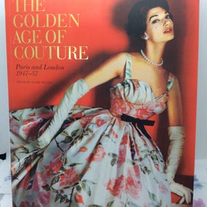 以下が含まれることがあります： クレア・ウィルコックス編集の書籍『The Golden Age of Couture: Paris and London 1947-57』。表紙には、花柄のドレスに黒いウエストリボン、長い白の手袋を着用した人物の写真が印刷されているハードカバーの本。