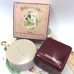 Puede incluir: Un set de polvos Baylis & Harding Victorian Collection con una caja de cartón cuadrada que presenta una ilustración vintage, un recipiente de polvos redondo beige con tapa moldeada y una caja cuadrada color burdeos oscuro.