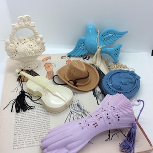 May include: A selection of vintage decorative items, including a white basket, a blue bird, a tan cowboy hat, a blue cameo, a violin, and a lavender glove. The items are arranged on a vintage magazine page.