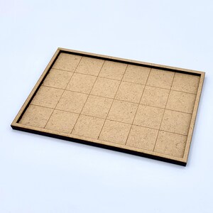 May include: A rectangular, light brown wooden tray with a grid pattern. The tray has a raised border and is divided into 25 equal squares. The wood has a natural, unfinished appearance.