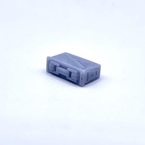 May include: A small, gray, rectangular metal box with a hinged lid and a latch. The box has a textured surface and appears to be made of metal.