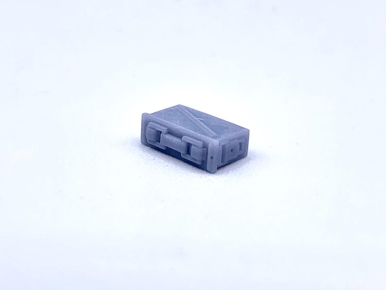 May include: A small, gray, rectangular metal box with a hinged lid and a latch. The box has a textured surface and appears to be made of metal.