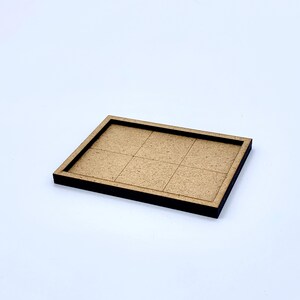 May include: A rectangular wooden tray with a dark brown border and a light brown interior divided into six equal squares. The tray is set against a white background.