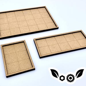 May include: Three wooden game board trays with grid patterns. The trays are rectangular with dark brown edges and a light brown interior. The sizes vary, with one large and two smaller trays. The background is white.