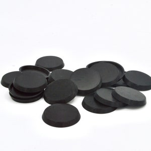 Pode incluir: Um monte de bases redondas de plástico preto para figuras em miniatura. As bases são de vários tamanhos e estão empilhadas umas sobre as outras.