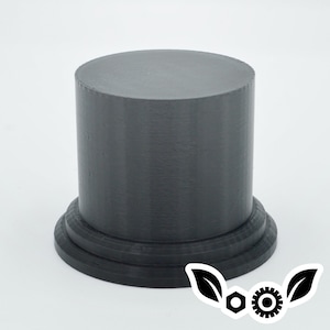 May include: A black, cylindrical pedestal with a smooth, rounded top and a slightly flared base. The pedestal is made of a textured material, possibly plastic or resin.