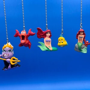 May include: Five colourful plastic figurines of characters from the Disney film The Little Mermaid hanging from silver chains. The characters include Ariel, Ursula, Sebastian, Flounder, and a red crab.