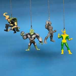 May include: Four superhero figurines hanging from chains. The figurines are of Loki, Hulk, Ultron, and Loki. The figurines are green, gray, and yellow.