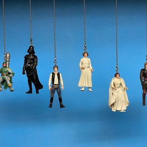 Puede incluir: Seis figuras de personajes de Star Wars colgando de cadenas plateadas. Los personajes incluyen Darth Vader, Han Solo, la princesa Leia, Boba Fett y dos versiones de la princesa Leia.