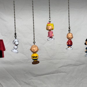 Peut inclure: Un ensemble de six chaines de tirage de ventilateur avec des personnages de Peanuts. Les personnages incluent Snoopy, Charlie Brown, Lucy, Linus, Sally et une niche rouge.