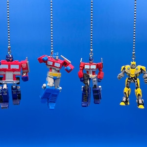 Può includere: Quattro action figure di Transformers appese a delle catene. Le figure sono Optimus Prime (rosso e blu), Bumblebee (giallo) e altri due Transformers in rosso e blu.