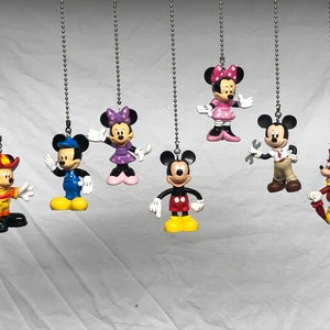 Może przedstawiać: Zestaw ośmiu kolorowych plastikowych figurek postaci z Disneya wiszących na srebrnych łańcuchach. Postacie obejmują Myszki Miki, Myszki Minnie, Kaczora Donalda, Goofy'ego, Pluto i inne. Figurki te idealnie nadają się do dodania odrobiny magii Disneya do każdego pokoju.