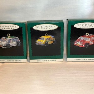 Op de afbeelding: Drie vintage Keepsake Ornament-dozen met miniatuur auto's. De dozen zijn groen met witte letters en de tekst "Keepsake Ornament" op de voorkant. De auto's zijn een witte bestelwagen, een gele schoolbus en een rode brandweerwagen.