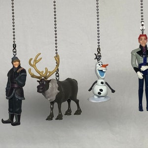 Puede incluir: Cuatro figuritas de personajes de Frozen colgando de cadenas plateadas. Los personajes son Olaf el muñeco de nieve, Kristoff, Sven el reno y Hans.