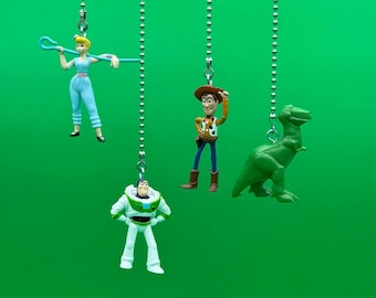 May include: Four Toy Story character figurines hanging from silver chains against a green background. The characters are Woody, Buzz Lightyear, Jessie, and the dinosaur Rex.