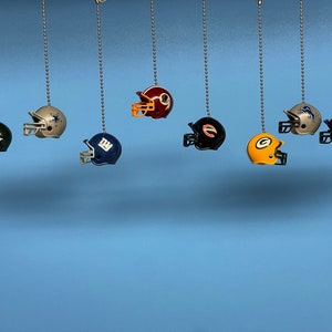 Peut inclure: Neuf casques de football miniatures suspendus à des chaînes. Les casques sont de différentes couleurs et présentent différents logos d'équipe, notamment les Eagles, les Cowboys, les Giants, les Patriots, les Bears, les Packers et les Vikings.