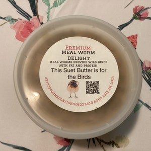 May include: A white plastic container with a brown lid. The lid has a label that says "Premium Meal Worm Delight" and "Meal Worms Provide Wild Birds With Fat and Protein". The label also says "This Suet Butter is for the Birds" and has a QR code.