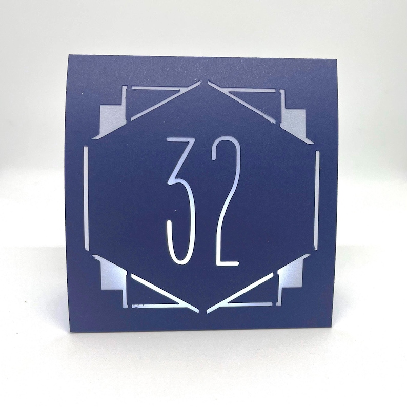 ART DECO Table Number LUMINARIES are made with sturdy card stock and sheer vellum paper. The numbers and modern design are cut out  so your battery tea lights can shine through.The glowing numbers make it easy for guests to find their table.