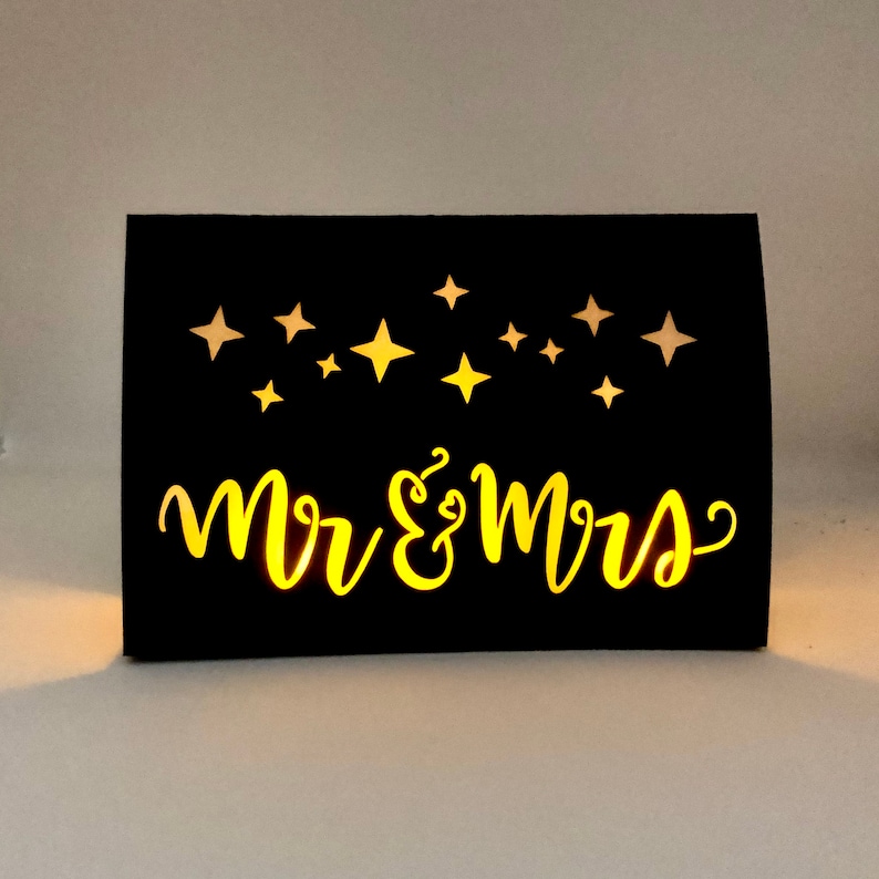 Star Design Night Table Number LUMINARIES are made with black card stock and sheer vellum paper. The Mr & Mrs design is cut out for use with LED tea lights can shine through (not included.) Available for free with a set of 1-10 Star Table Numbers.