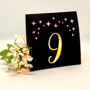 Star Design Night Table Number LUMINARIES are made with black card stock and sheer vellum paper. The number and design is cut out for use with LED tea lights can shine through (not included.) The glowing numbers make it easy for guests to find their table.