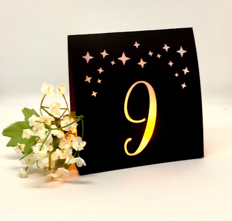 Star Design Night Table Number LUMINARIES are made with black card stock and sheer vellum paper. The number and design is cut out for use with LED tea lights can shine through (not included.) The glowing numbers make it easy for guests to find their table.