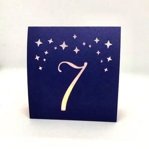 Star Design Night Table Number LUMINARIES are made with navy card stock and sheer vellum paper. The number and design is cut out for use with LED tea lights can shine through (not included.) The glowing numbers make it easy for guests to find their table.