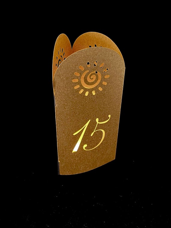 SUNNY TOWER Table Number Luminaries are 3-sided cutout arches. Colors include kraft, cream, blush, or light purple.
