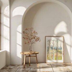 May include: A watercolor painting of birch trees in a wooden frame, displayed in a bright room. A small wooden table holds a clear glass vase with dried branches. The room has arched doorways and a window.