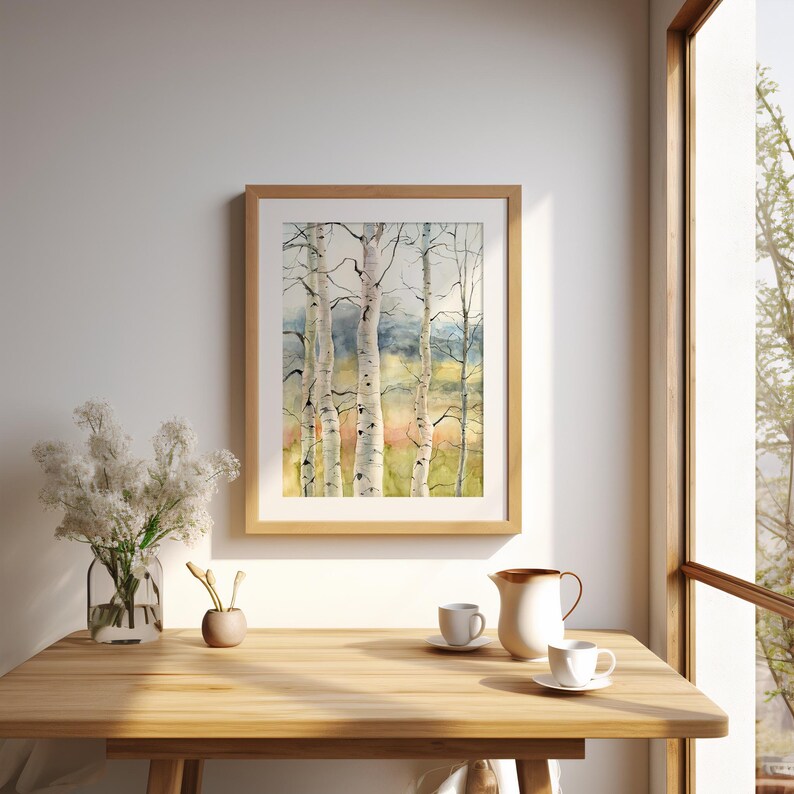 May include: A framed watercolor painting of birch trees with white bark and black markings. The artwork is displayed on a wooden table, alongside a vase of white flowers, a small vase, and a coffee set. The painting has a light brown wooden frame.