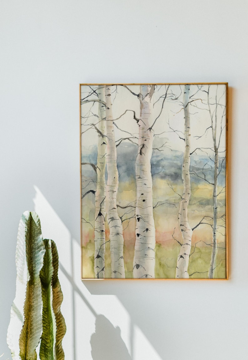 May include: Watercolor painting of birch trees in a gold frame. The trees have white bark with black markings and are set against a backdrop of soft greens, yellows, and blues. The artwork is displayed on a white wall.