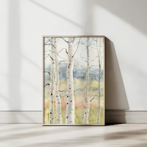 May include: A framed watercolor painting of birch trees. The artwork features several white-barked trees with dark branches against a soft, blurred background of green, blue, and yellow hues. The frame is a light, natural wood color.