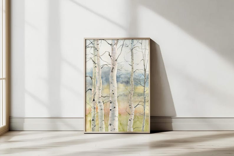May include: A framed watercolor painting of birch trees. The artwork features several white-barked trees with dark branches against a soft, blurred background of green, blue, and yellow hues. The frame is a light, natural wood color.