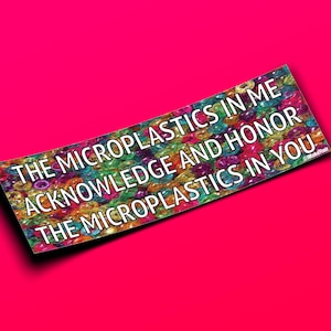 May include: A rectangular sticker with the text "THE MICROPLASTICS IN ME ACKNOWLEDGE AND HONOR THE MICROPLASTICS IN YOU" in white letters. The background of the text is a colorful pattern of small, round shapes. The sticker is set against a bright pink background.