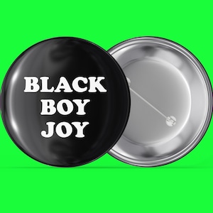 May include: Black button pin with the text "BLACK BOY JOY" in white letters on a black background. The back of the pin is silver.