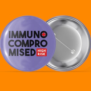 Könnte beinhalten: Lilafarbener Knopf mit dem Text "Immunsupprimiert Hohes Risiko" in schwarzer und roter Schrift. Die Rückseite des Knopfes ist silber.