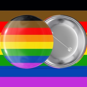 May include: A rainbow pride flag pin with a brown, red, orange, yellow, green, blue, and purple stripe design. The pin is on a white background.