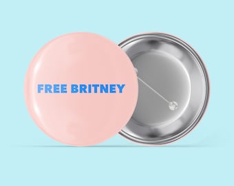 May include: A pink button with the text "FREE BRITNEY" in blue lettering. The back of the button is silver with a pin.