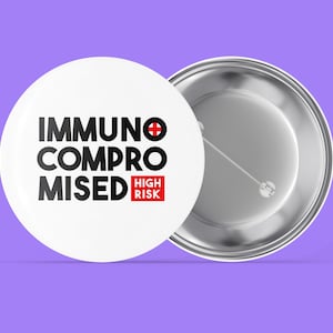 Könnte beinhalten: Weißer Knopf mit schwarzem Text, der "Immunsupprimiert Hohes Risiko" mit einem roten Kreuzsymbol lautet. Die Rückseite des Knopfes ist silber.