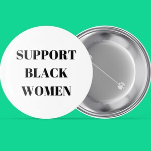 Op de afbeelding: Een witte knop met de tekst "SUPPORT BLACK WOMEN" in zwarte letters. De achterkant van de knop is zilver.