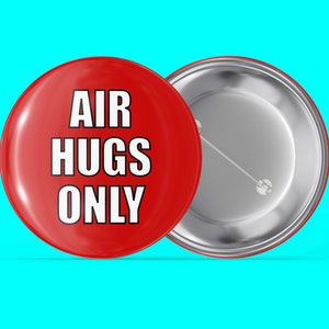 May include: Red button with white text that reads "AIR HUGS ONLY". The back of the button is silver.