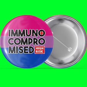 Könnte beinhalten: Ein runder Knopf mit rosa, lila und blauem Hintergrund. Der Text "IMMUNO COMPROMISED HIGH RISK" ist in schwarzen Buchstaben auf dem Knopf gedruckt.