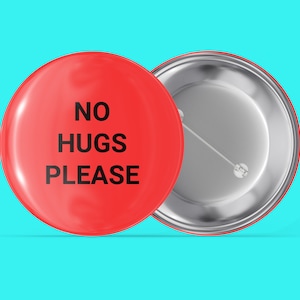 Könnte beinhalten: Ein roter Knopf mit dem Text "NO HUGS PLEASE" in schwarzen Buchstaben. Die Rückseite des Knopfes ist silber.