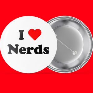 Op de afbeelding: Een witte knop met een rood hart en de tekst "I ♥ Nerds" in zwart. De knop is bevestigd aan een zilveren pin.