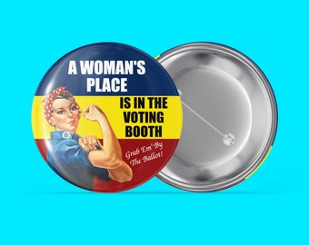 May include: A round button with a retro design. The button features a woman flexing her arm with the text "A Woman's Place Is In The Voting Booth." The button has a blue, yellow, and red color scheme. The text "Grab Em' By The Ballot!" is also included.